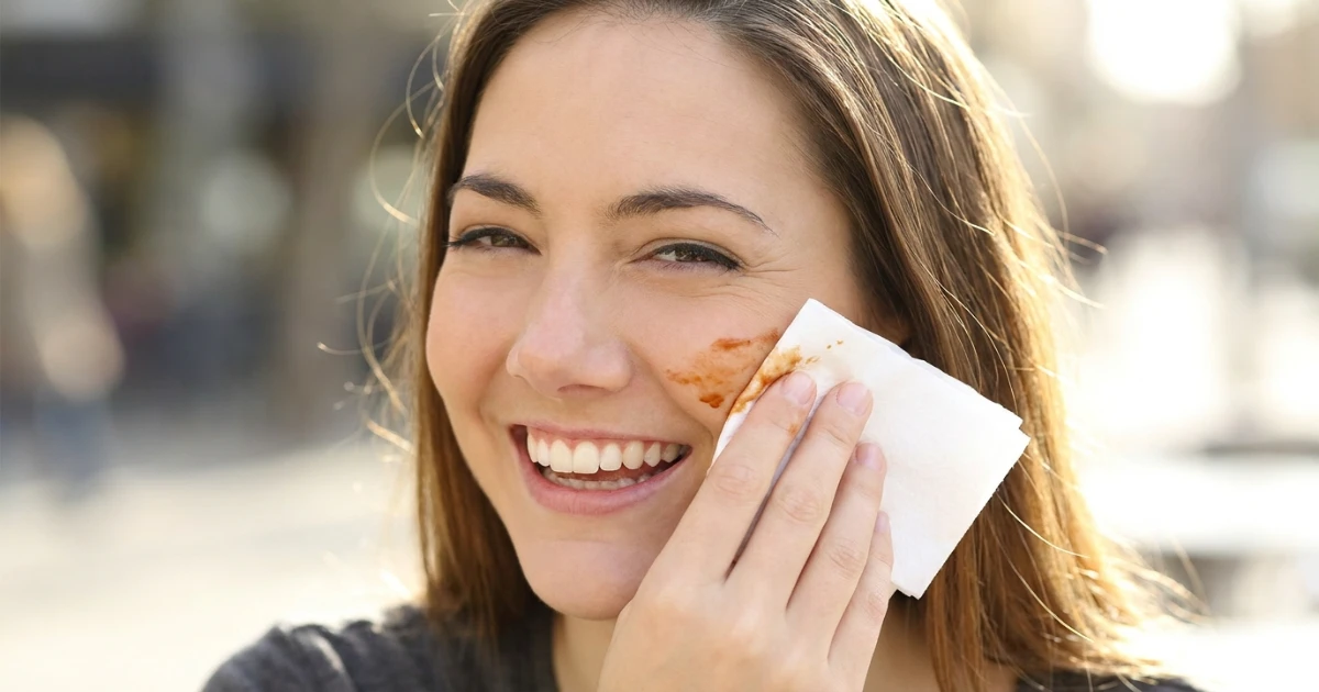Person smiling while wiping sauce off their cheek